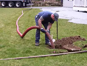 Septic pumping technician servicing a residential septic tank with a vacuum hose in Andover, MA