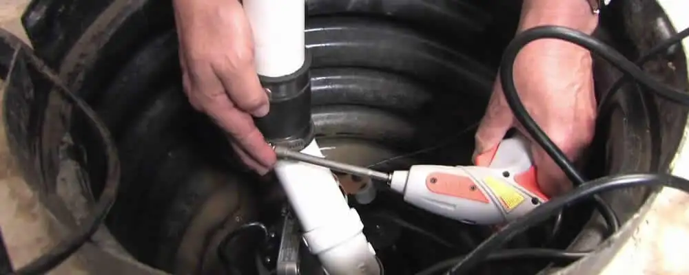Sump pump installation technician connecting PVC discharge piping in Andover, MA