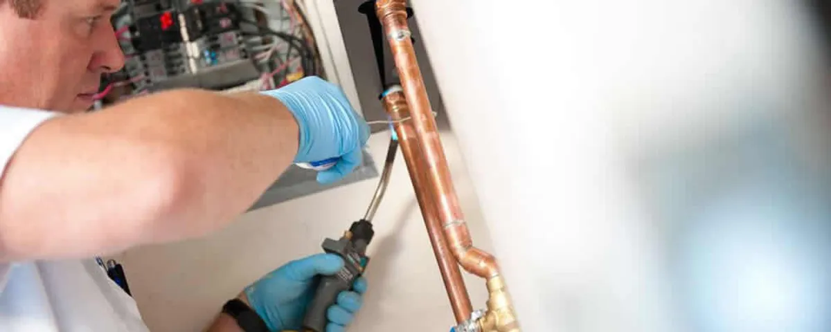 Water heater repair technician testing copper pipe connections and controls in Andover, MA