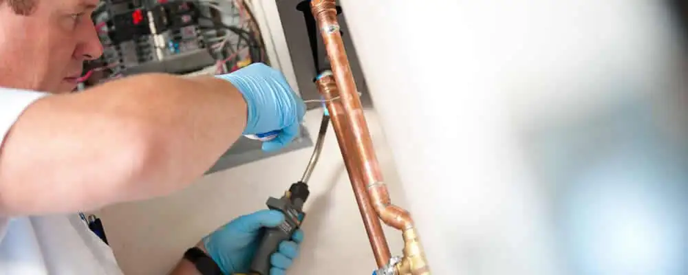 Water heater repair technician testing copper pipe connections and controls in Andover, MA